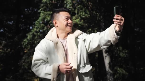 Číňan nahrávání video zprávy pro přítele při pohledu na jeho telefon venku. — Stock video