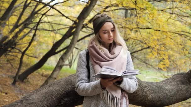 Жінка-доросла дівчина стоїть у осінньому лісі з жовтим листям, що читає книгу про природу. "Красуня відпочиває і відпочиває з книгою в руках". Блондинка блакитних очей навчається на відкритому повітрі. Натхнення — стокове відео