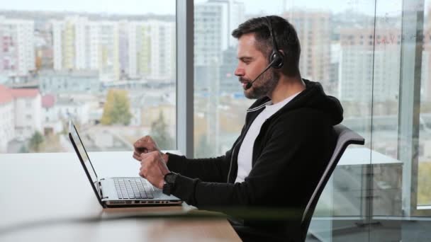 Heureux jeune homme d'affaires porte casque parle à l'ordinateur portable de la caméra Web faisant appel à la vidéoconférence en ligne à distance. courtier Internet masculin faisant chat à distance de travail à partir du bureau. Vue Webcam. — Video