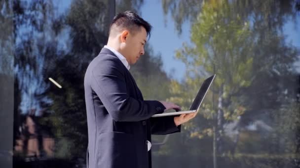 Asiatischer Mann schaut auf den Bildschirm von Laptop und SMS-Nachricht im Freien. — Stockvideo