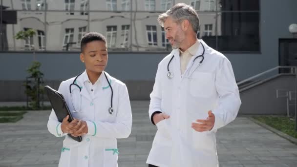 Médico caucasiano conversando com colega afro-americano durante a pausa para o trabalho. — Vídeo de Stock