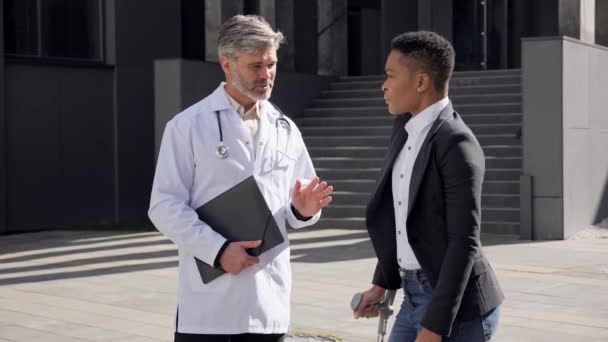 Cirujano consultando paciente con pierna rota en la calle cerca del centro médico. — Vídeo de stock