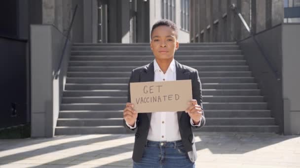 Zwarte vrouw protestantse tribunes met teken krijgen gevaccineerd geschreven op karton. — Stockvideo