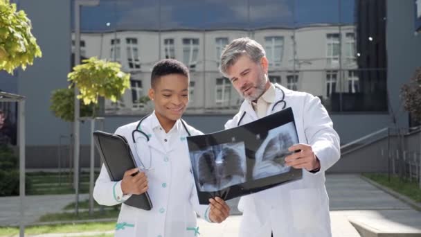 Два лікарі обстежують рентгенівські легені під час епідемії COVID 19 поблизу лікарні . — стокове відео