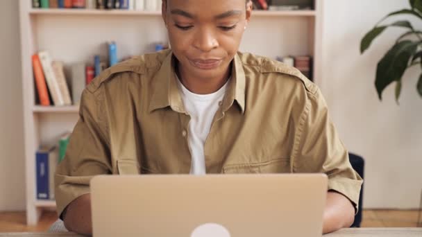 Εστιασμένη Αφροαμερικανή γυναίκα που χρησιμοποιεί φορητό υπολογιστή ενώ κάθεται στο χώρο εργασίας στο σπίτι. — Αρχείο Βίντεο