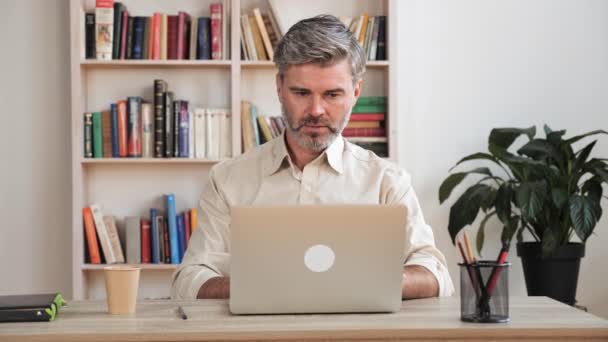Orta yaşlı bir adam internet üzerinden mi çalışıyor yoksa evde bilgisayarla mı çalışıyor?. — Stok video