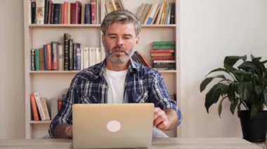 Yakışıklı orta yaşlı adam iş yerinde otururken dizüstü bilgisayarda işini bitiriyor..