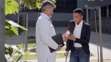 Beyaz elbiseli aile doktoru bacağı kırık hastaya ilaç veriyor..