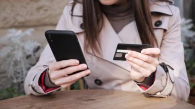 Kadın eli, elinde banka kartı, cep telefonuyla CVV kodunu giriyor..