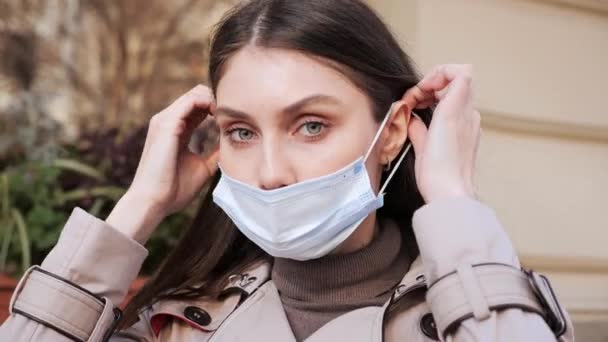 Mooie glimlachende jonge vrouw zet gezichtsmasker om te beschermen tegen coronavirus. — Stockvideo