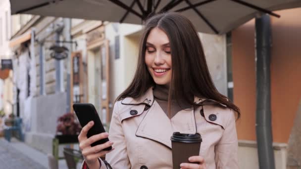 Mulher mensagens de texto em Smartphone beber café enquanto olha na câmera. — Vídeo de Stock