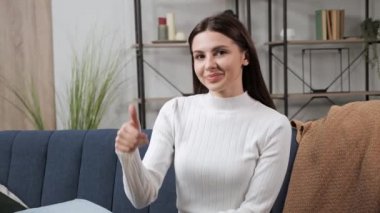 Kız, evdeki kanepede oturan kameraya baş parmak hareketi yapıyor..