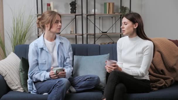 두 젊은 백인 여자 가 거실에서 소파에 앉아 차를 마시며. — 비디오