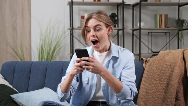 Señora sorprendida celebrando la victoria en el teléfono inteligente en el apartamento. — Vídeos de Stock