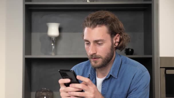 Man zit thuis in de keuken te scrollen flirten in social media. — Stockvideo