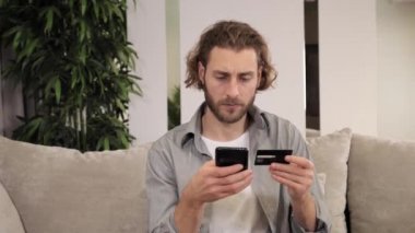 Evde alışveriş yapan yorgun genç adam, kredi kartıyla online alışveriş yapıyor.. 