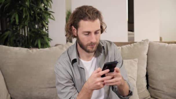 Positieve man houden met behulp van smartphone kijken naar sociale media thuis. — Stockvideo