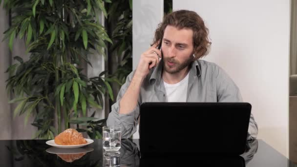 Homem bonito usando laptop e smartphone ter telefonema falando. — Vídeo de Stock