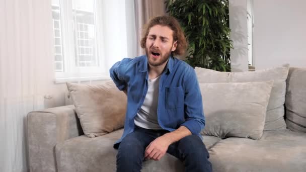 Ung forretningsmand føler sig tilbage og nakkesmerter hjemme på sofaen. – Stock-video
