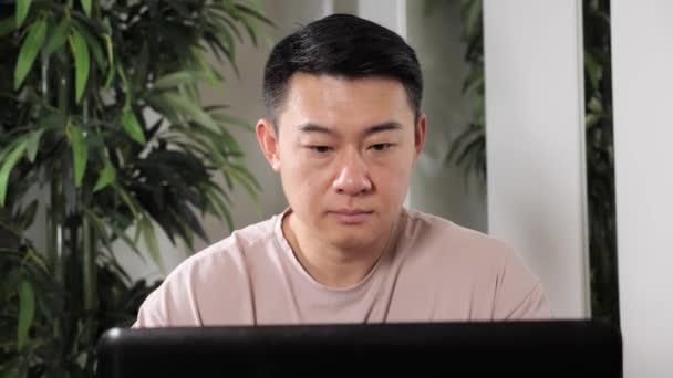 若いですアジアのフリーランスの男作業上のコンピュータにホーム遠くの仕事. — ストック動画