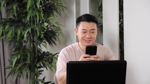 Adulto guapo asiático hombre sentado en la mesa de trabajo usando smartphone remoto trabajo. — Vídeo de stock
