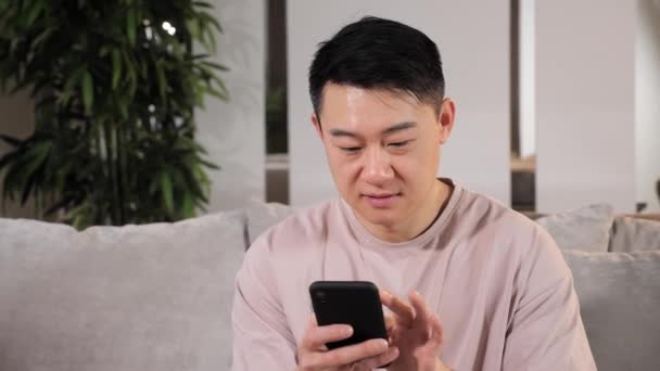Hombre asiático usando el teléfono móvil, hojeando el desplazamiento que golpea a través de Internet. — Vídeos de Stock