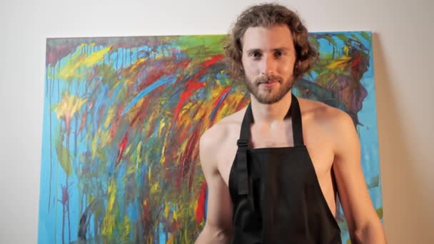 Porträt eines Künstlers auf einem Hintergrund von Gemälden in seinem Atelier. — Stockvideo