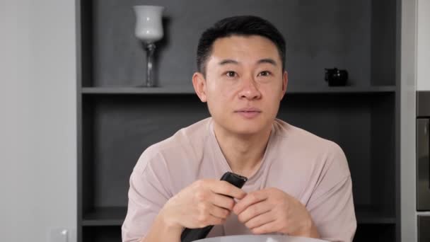 De olhos abertos jovem asiático homem assistindo TV e comer milho pop em casa. — Vídeo de Stock