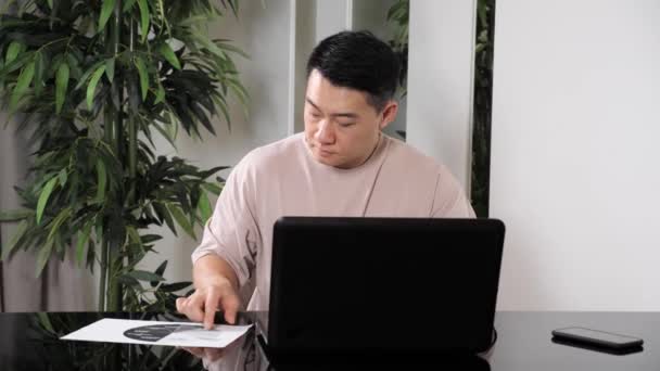 Азіатський бізнесмен перевіряє корпоративні паперові діаграми, сидячи вдома. — стокове відео