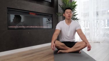Yakışıklı Asyalı adam evde yoga yapıyor. Basit vücut lotusunda dinleniyor..
