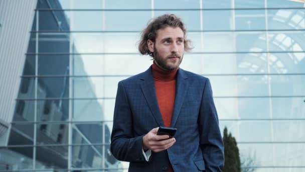 Γενειοφόρος επιχειρηματίας σε ένα κοστούμι χρησιμοποιεί ένα Smartphone σε ένα δρόμο στο κέντρο της πόλης. — Αρχείο Βίντεο