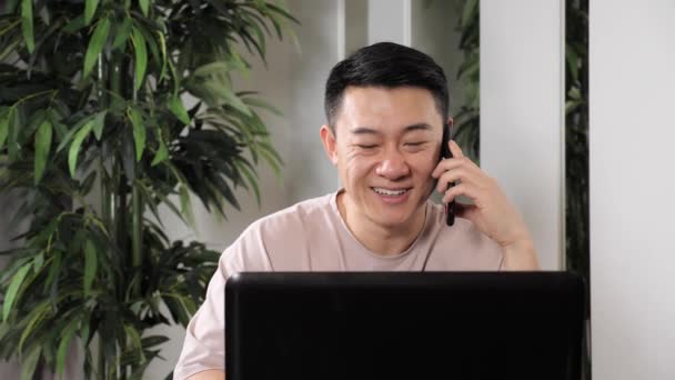 Primer plano asiático sonriendo hombre hablando en móvil en casa oficina. — Vídeo de stock