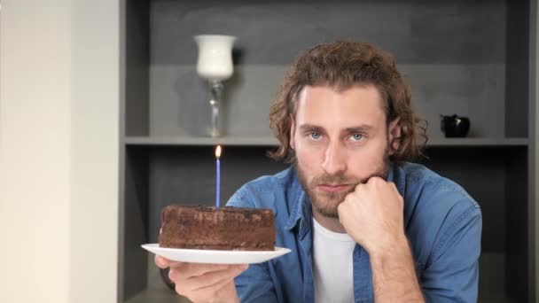 坐在家里厨房里抱着生日蛋糕伤心的眼睛的家伙. — 图库视频影像