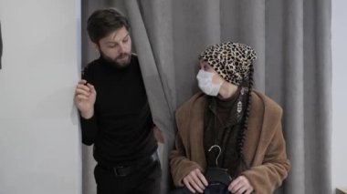 Kadın soyunma odasının yanında duruyor. Alışveriş merkezinde kocası için bir ceket tutuyor.. 