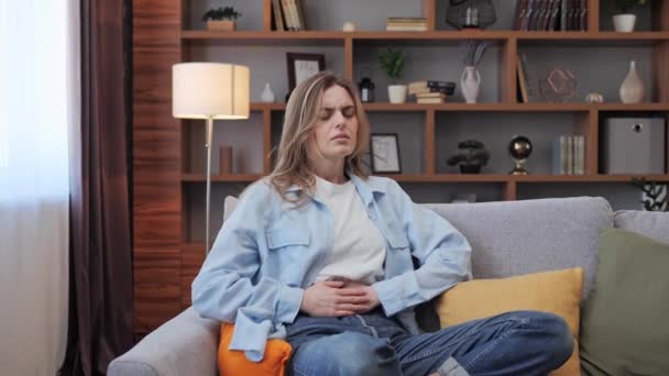 Woman feels pain in upper abdomen, symptom of gastritis, indigestion, closeup. Sick girl suffering from stomach ache sitting in bed, holding belly, feeling abdominal or menstrual pain in morning. — Stock Video