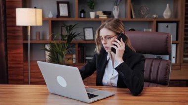 Akıllı, kendine güvenen bir iş kadını iş ortağıyla telefonda konuşuyor. Telefon görüşmeleri sırasında kadın profesyonel jestler. Ciddi bir iş kadını dizüstü bilgisayara bakıyor..