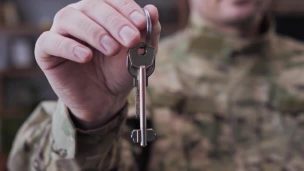 Vista de perto do soldado homem satisfeito usando uniforme de camuflagem segurando a chave nas mãos, estando feliz em comprar nova compra, casa ou apartamento. O homem voltou para casa depois da guerra. Apoio estatal. — Vídeo de Stock