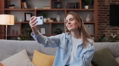 Yetişkin sarışın kadın kanepede otururken bir video görüşmesi yapıyor, gülümsüyor ve ailesiyle konuşuyor. İş kadını, merkez ofisteki ekiple çevrimiçi görüşme hakkında görüntülü konuşma yapıyor..