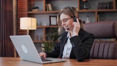 Milenyum işkadını ofis masasında kulaklık takarak oturuyor. Telekonferans yoluyla müşteriyi dinliyor. Uzaktan pazarlık yapıyor..