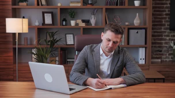 Επαγγελματίας Δημιουργικός Επιχειρηματίας Καθισμένος στο χώρο εργασίας του στο στούντιο Home Office Εργάζεται σε ένα Laptop Χρησιμοποιώντας Laptop, γράψτε ιδέες στο Notepad. Ο άνθρωπος τελειώνει σε απευθείας σύνδεση συνεδρίαση αναθεώρηση σημειώσεις σκέψης. — Αρχείο Βίντεο