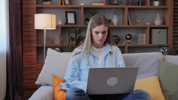 Jonge nerveuze vrouw zit op de bank terwijl ze thuis aan een laptop werkt. Ze krijgt slecht nieuws, raakt van streek voelt stress en hopeloosheid. mooi meisje freelancer hebben onverwachte problemen voelt gespannen. — Stockvideo