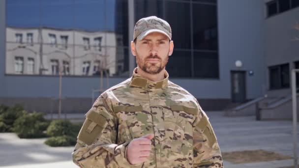 Soldat militaire confiant montrant le pouce debout à l'extérieur. Portrait d'un beau jeune soldat en casquette regardant la caméra. Gros plan de l'homme sérieux face à l'extérieur en ville. Uniforme militaire. — Video