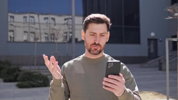 Happy attractive guy enjoying video conversation outside. Young man in casual clothes talking through video call app online using mobile phone. Businessman gesturing with hands during a video call. — Stock Video