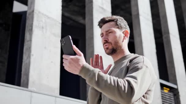 Online Video Call Ritratto di bello giovane uomo elegante in abiti casual Parlare con amici o colleghi mentre in piedi fuori sulla City Street. Mano ondulata nell'ambiente urbano. Tecnologia moderna. — Video Stock