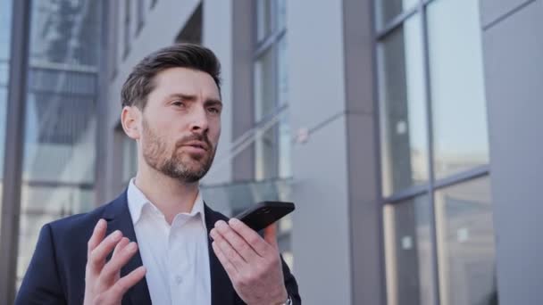 スピーカーの電話で顧客に携帯電話の話を保持超高層ビルのオフィスの近くを歩く良い探している男性起業家成功したビジネスマンは、ボイスメールを送信し、現代の技術コンセプト. — ストック動画