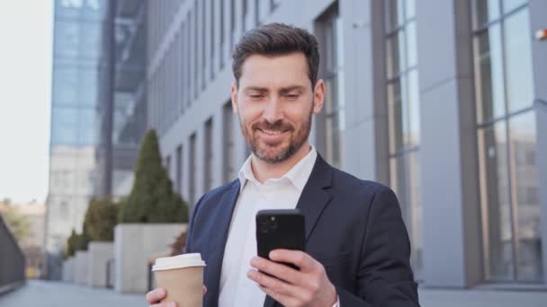 Close up view of happy business man uses phone drinks coffee good news wspaniałe emocje wygrywa w centrum smsowania przewijanie podsłuchiwanie smartfona świetna technologia rano komunikacji online. — Wideo stockowe