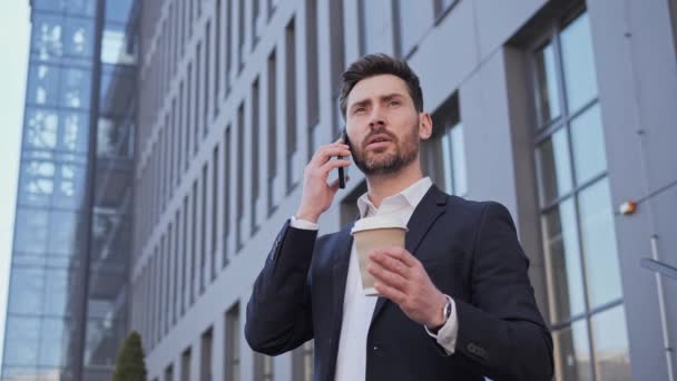 Un hombre de negocios inteligente y seguro hablando por teléfono móvil en el centro de oficinas. Hombre sosteniendo taza de café de pie al aire libre mientras habla por teléfono inteligente. Telecomunicaciones y redes móviles para el concepto empresarial. — Vídeo de stock