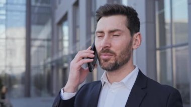 Dışarıda telefonla konuşan yakışıklı bir adam portresi. İş adamı şehir merkezinde akıllı telefondan konuşuyor. Konsantre sakallı adam dışarıdaki telefonu arıyor. Ofis çalışanı dışarıda cep telefonuyla konuşuyor..