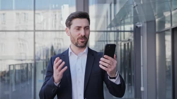 Позитивный бизнесмен, делающий онлайн видеочат, используя приложение для мобильного телефона, выглядит уверенным вне офиса, стоящего на городской улице. Деловые люди цифровые технологии. Финансы. — стоковое видео