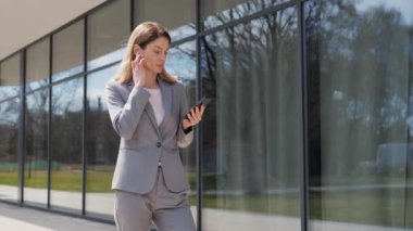 Akıllı telefondan konuşan zarif bir iş kadını kablosuz kulaklık kullanıyor. Dışarıdaki cep telefonundan kendine güvenen bir iş kadını arıyor. Ofis merkezine yakın bir yerde ciddi bir kadının resmi var..